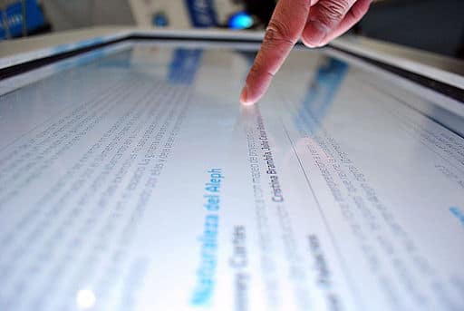 A finger interacts with a large interactive screen.